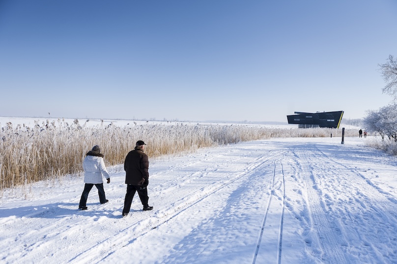 Het Natuurbelevingcentrum als zwart baken in een besneeuwd winterlandschap